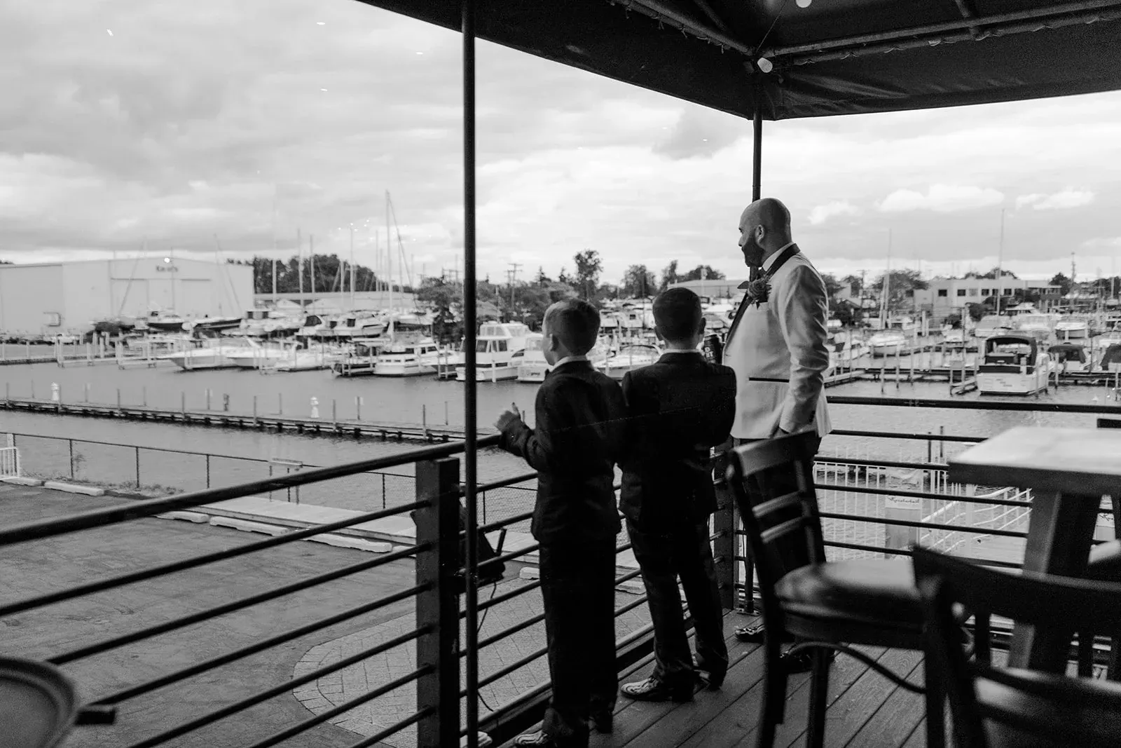 A groom and two boys on The Club's deck looking out over the marina, black and white