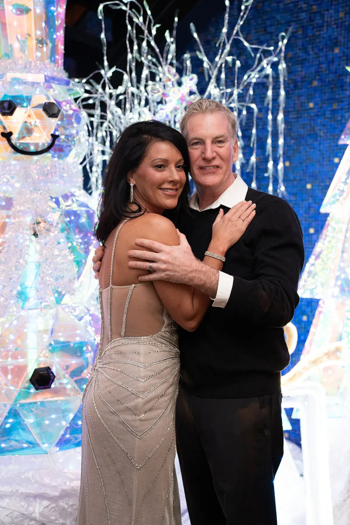 A couple between white Christmas trees at a holiday party