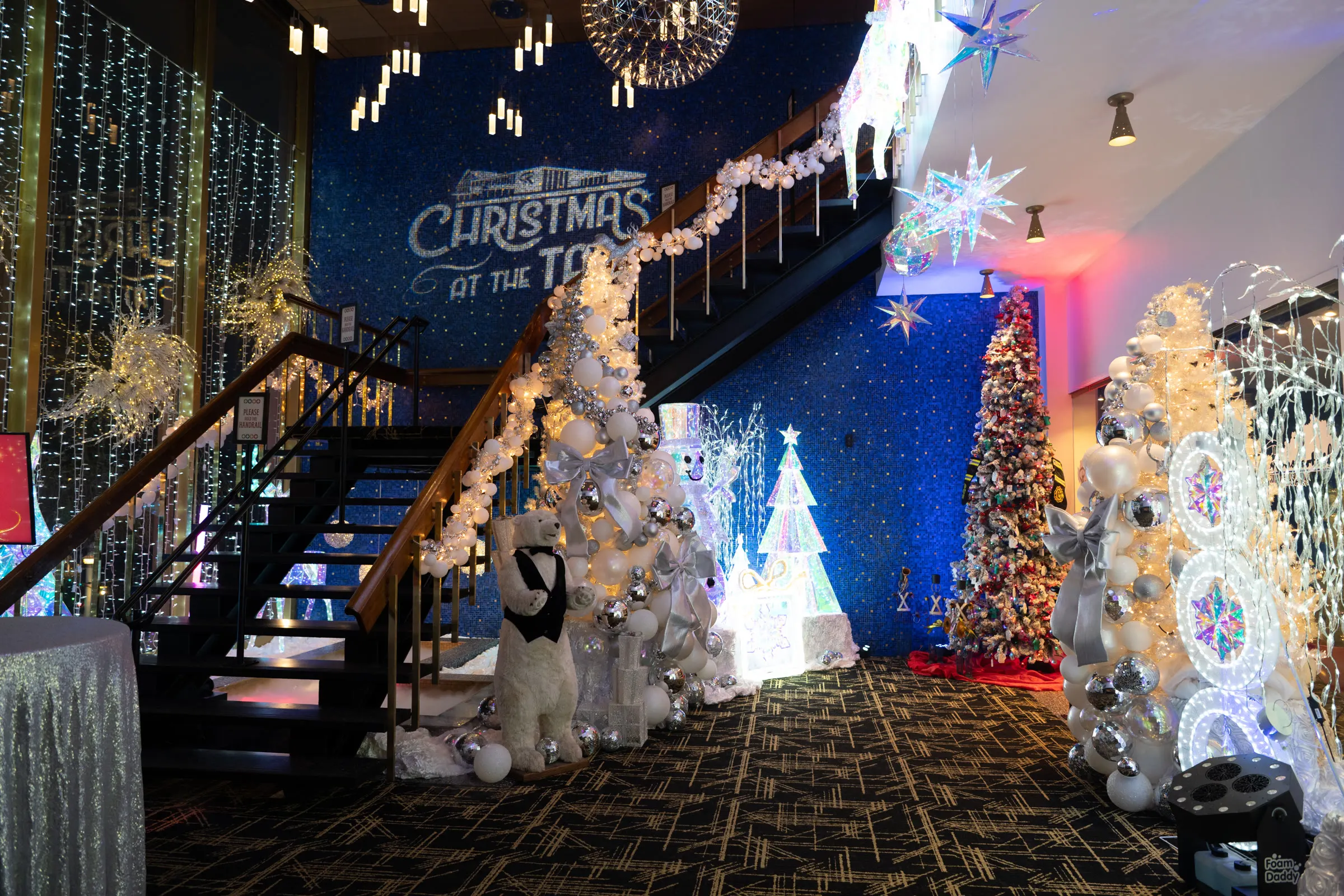 The lobby staircase lined with white lit Christmas trees under the Christmas at the Tail sign